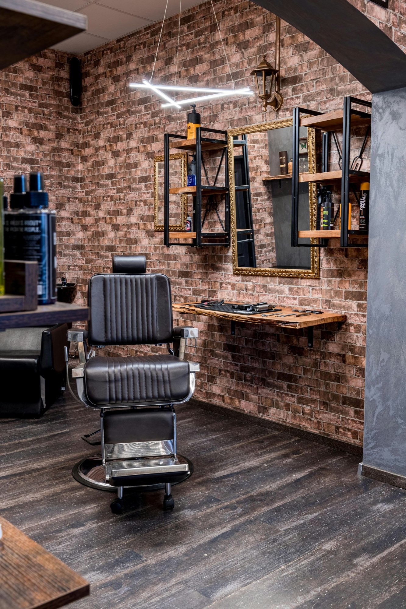 A barber chair beneath a gold-framed mirror, tools laid out on a wood ledge