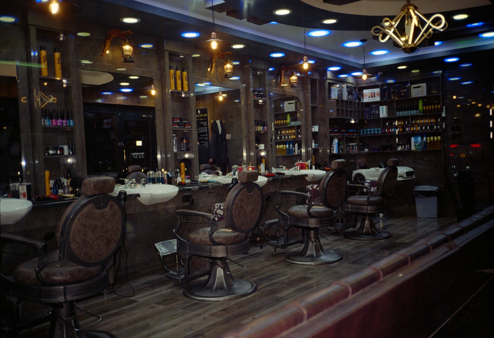 A row of barber chairs facing lit mirrors in a dim, warmly lit shop