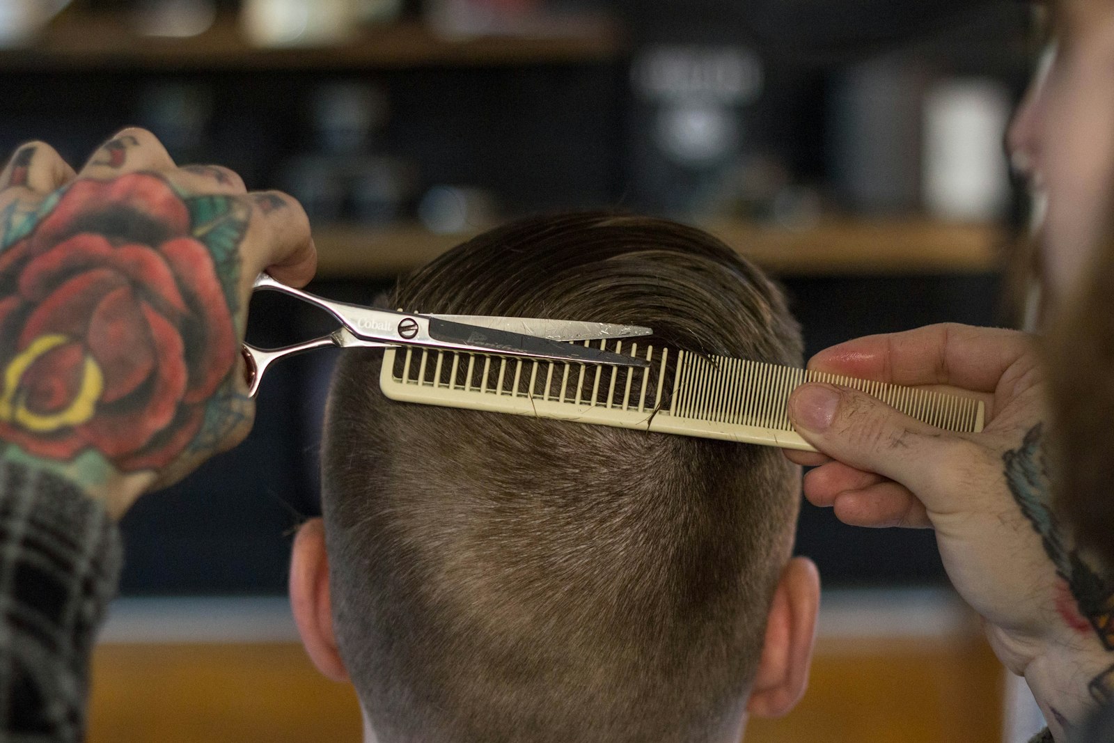 Barber's hands guiding a comb and shears through a client's hair
